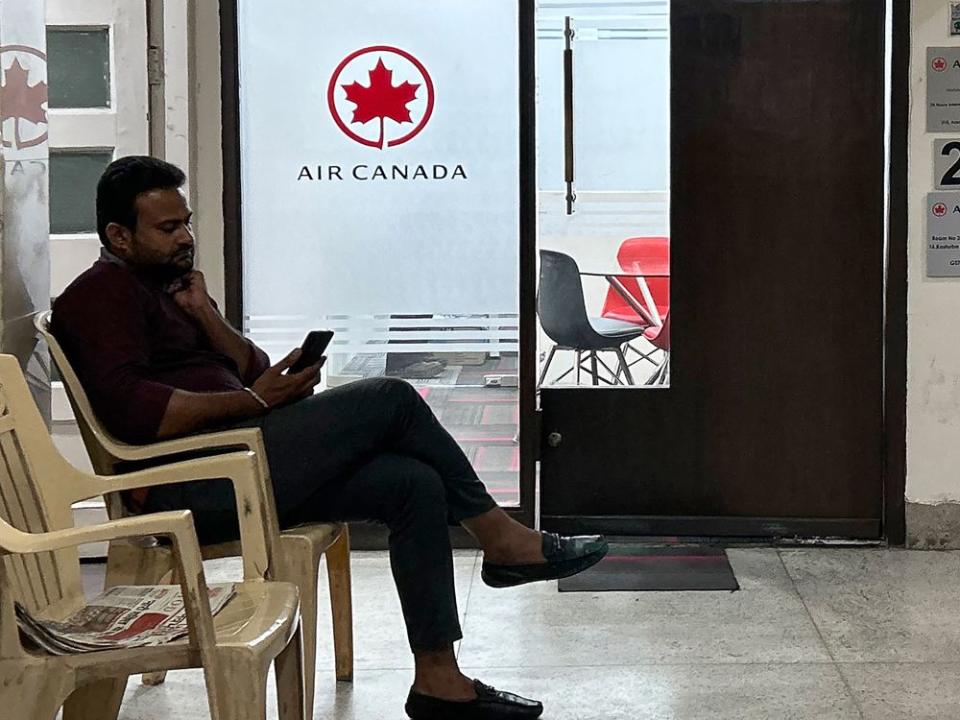 A man checks his mobile as he sits outside an Air Canada Inc. regional office in New Delhi, India.