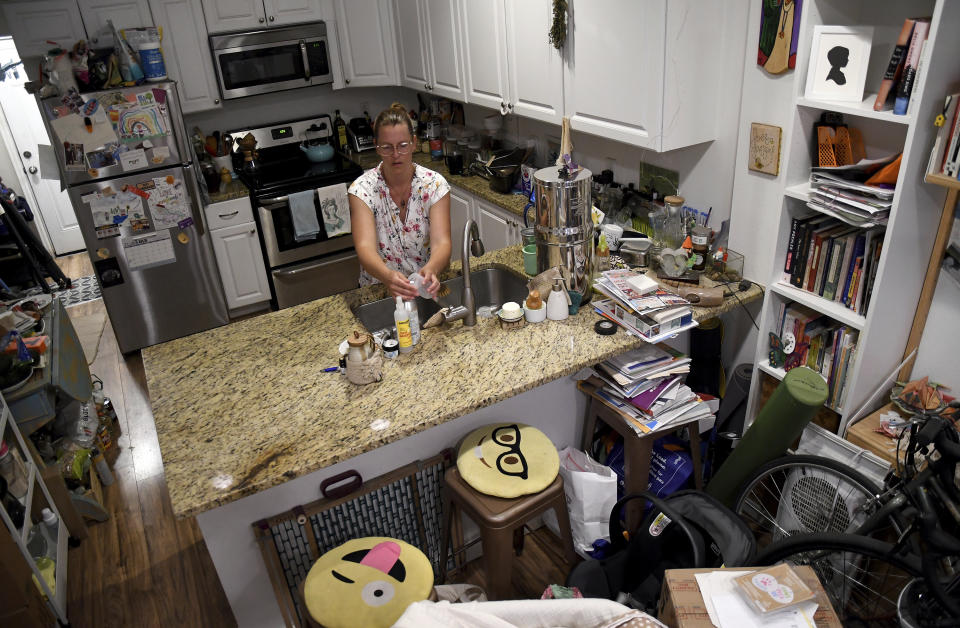 Amanda Morian washes dishes in her home in Denver's Globeville neighborhood on Monday, July 24, 2023. Morian, who has a 13-week-old baby susceptible to hot weather, is desperate to keep the house cool. She bought thermal curtains, ceiling fans and runs a window unit. At night, it's too hot to swaddle her newborn, but she tries to do skin-to-skin touch to regulate the baby's body temperature. Morian said that even with subsidies, she can't afford to install air conditioning. (AP Photo/Thomas Peipert)