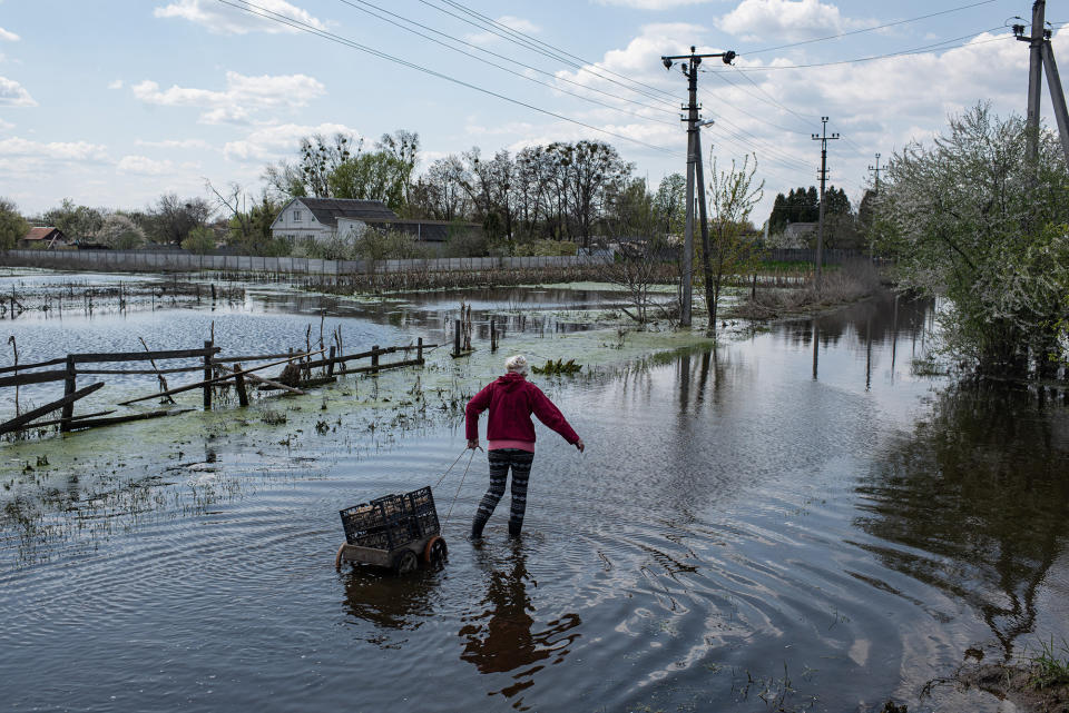 A local resident named Nadiia pulls a cart with crates filled with potatoes through a flooded street in Demydiv, Ukraine, on May 2, 2022. To keep Russian armored columns at bay, Ukrainian forces released water from a nearby hydroelectric dam to intentionally flood Demydiv, a village north of Kyiv.