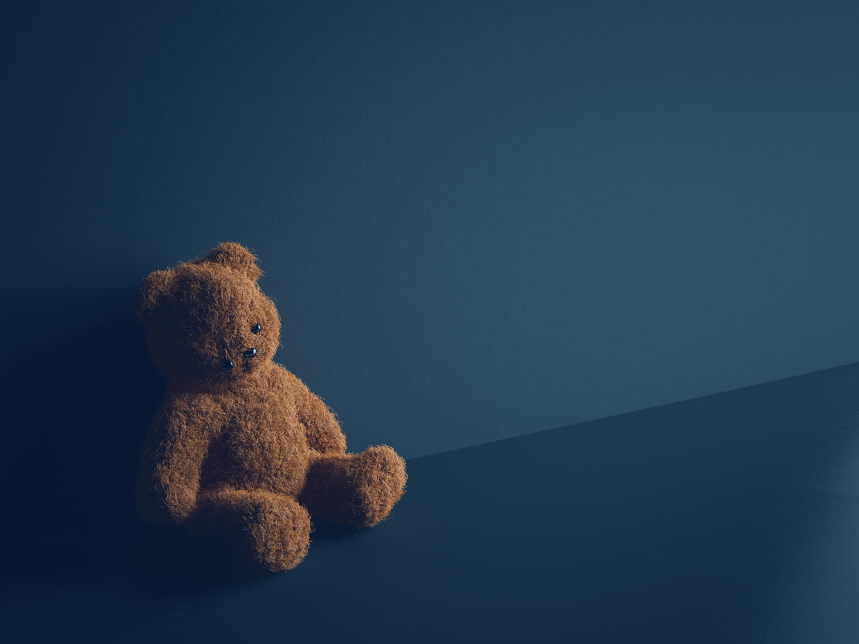 Teddy bear with torn eye sits in dark room. Child abuse and violence concept.