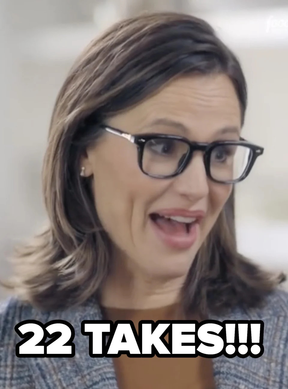 Jennifer Garner smiles, wearing glasses and a checked blazer, in a kitchen setting