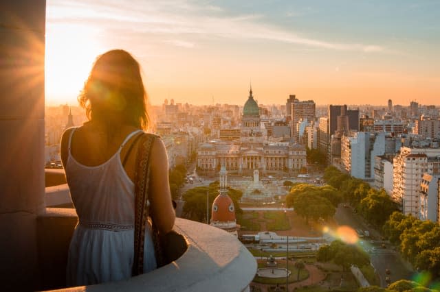 Rear View Of Woman Standing At Balcony Against Cityscape During Sunset