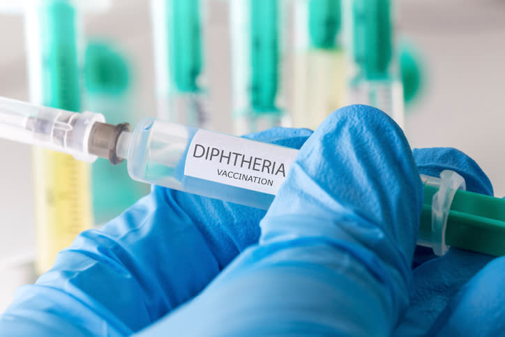 A doctor holding a syringe that says "Dipththeria"