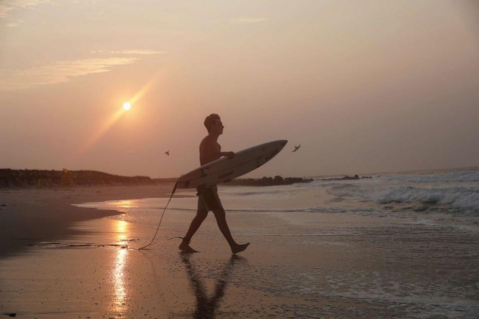 PHOTO: A surfer carries his board into the Atlantic Ocean during a hazy sunrise from the wildfires in Canada in Lido Beach, New York, July 18, 2023. (Shannon Stapleton/Reuters)