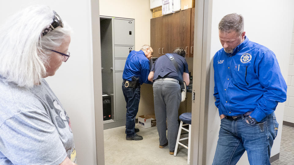 Marion County Record reporter Phyllis Zorn and Sheriff Jeff Soyez stand outside the evidence room where an undersheriff signs over newspaper property to a forensic expert.