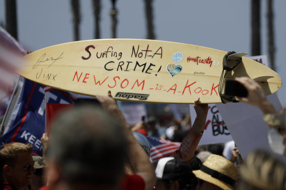 A protestor holds a hand painted sign on a surfboard during a May Day demonstration at the pier, Friday, May 1, 2020, in Huntington Beach, Calif. (AP Photo/Chris Carlson)