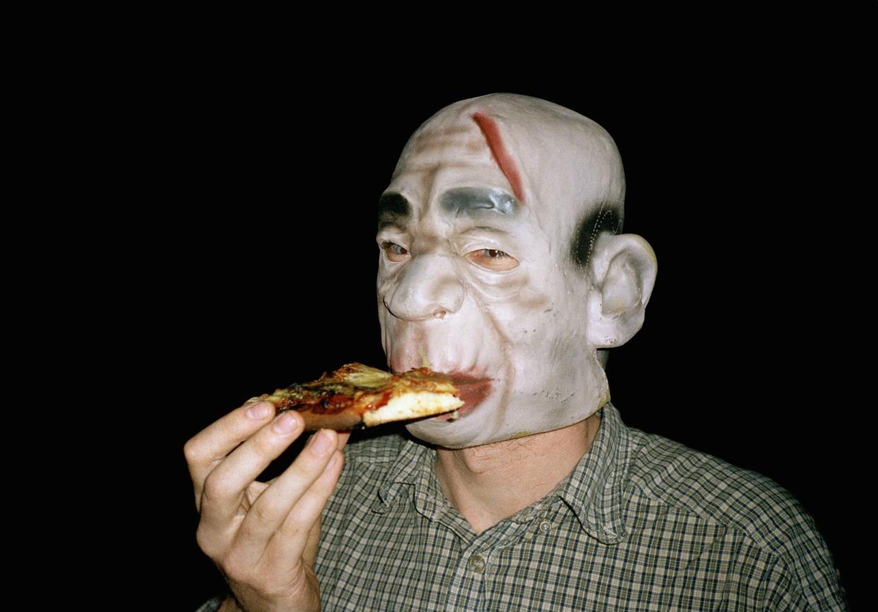 Man wearing rubber monster mask and eating pizza
