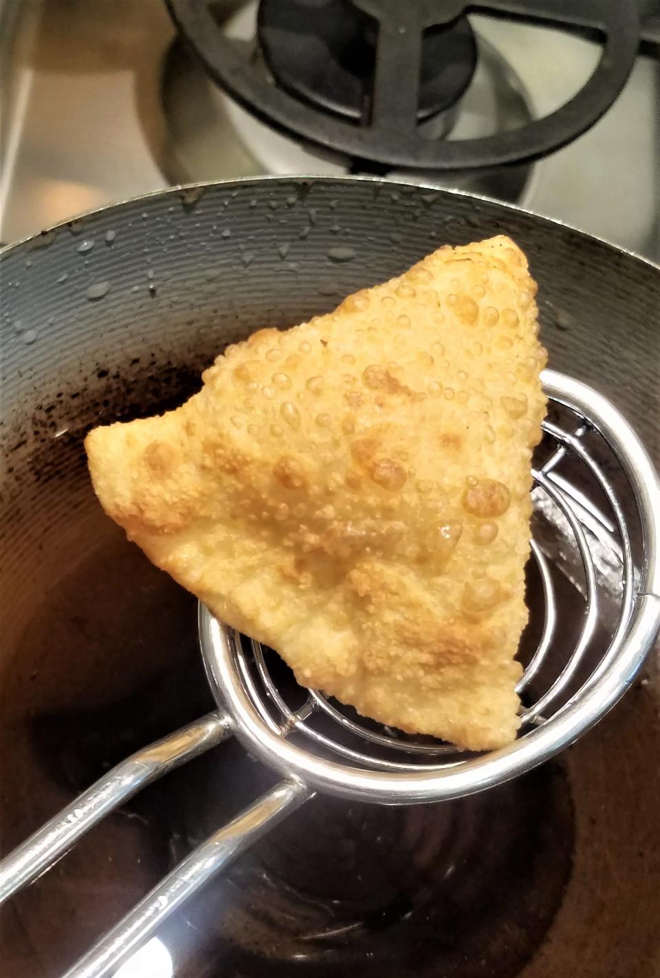 A finished samosa, fried crispy, filled with warm spiced potatoes.