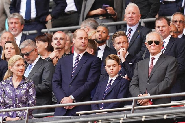 Prince William and Prince George watch the football from a stand. Both wear blue suits.