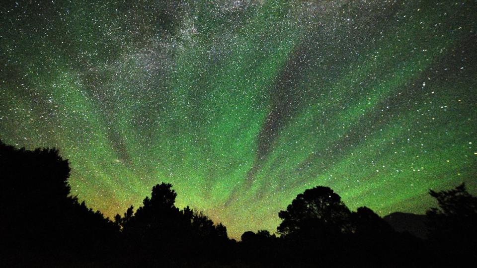 Green streaks of light shine in the night sky full of stars