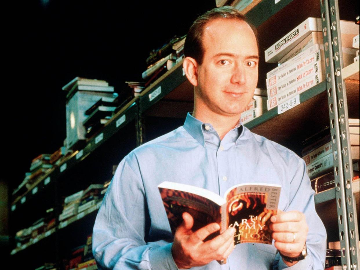 Jeff Bezos holds book and poses against book rack