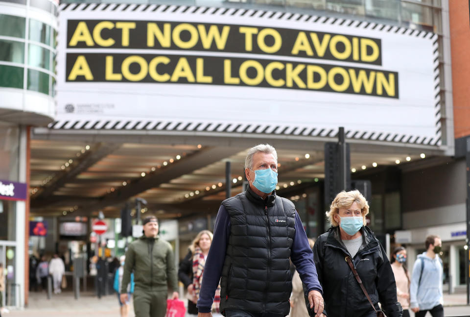 People wearing face masks walk past a advertisement on Market Street in Manchester, as the city is waiting to find out if the region will be placed into the Very High category with tier 3 lockdown restrictions to curb the spread of coronavirus. (Photo by Martin Rickett/PA Images via Getty Images)