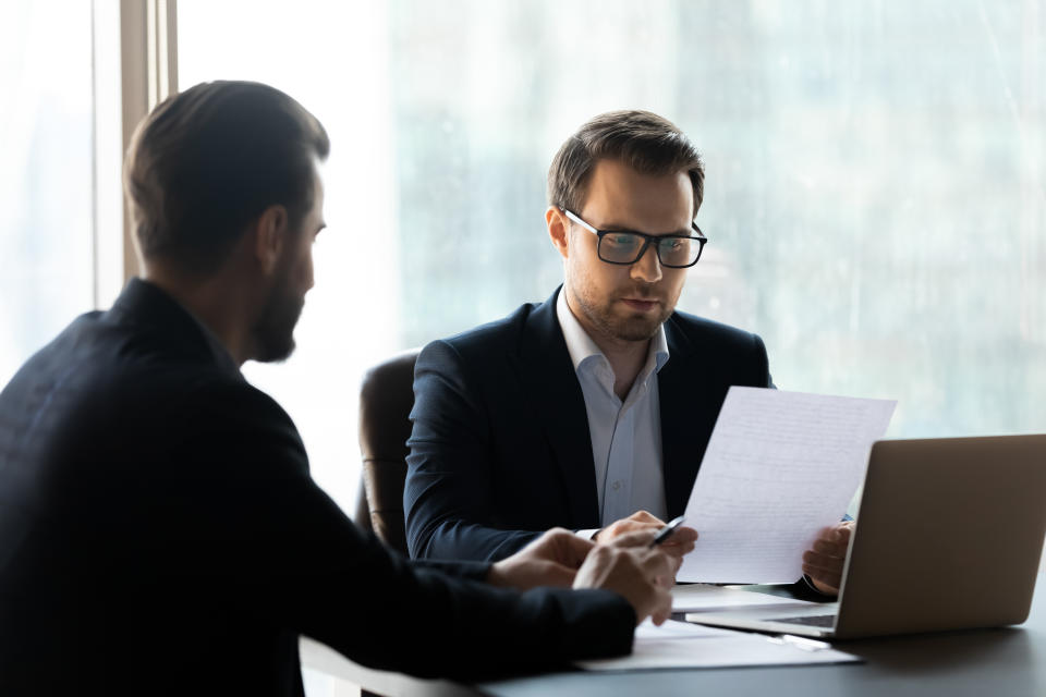 Serious businessman reading cv new job candidate and using laptop. Handsome young leader listening terms of transaction from partner. Difficult business decision about make corporate deal.