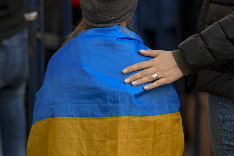 A woman puts her hand on the back of a child draped in the Ukrainian flag during a protest against Russia's war in Ukraine, in front of the Russian embassy in Bucharest, Romania, Sunday, March 27, 2022. (AP Photo/Andreea Alexandru)