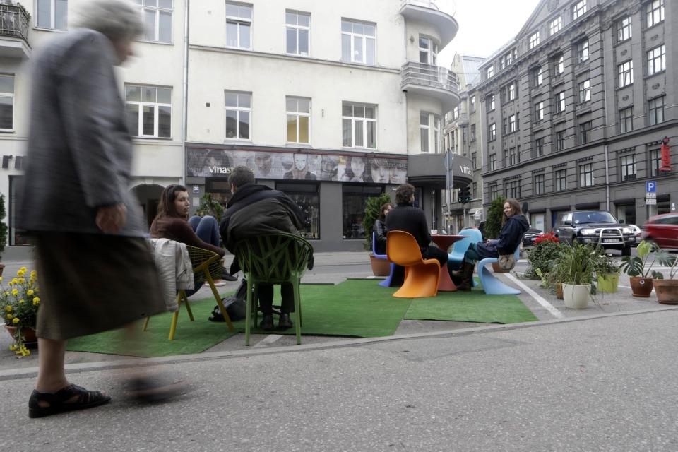 A woman walks past people participating in a PARK(ing) Day event in Riga