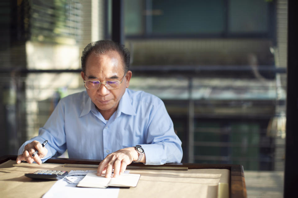 Elderly Taiwanese man sitting by the table and managing his home finances.