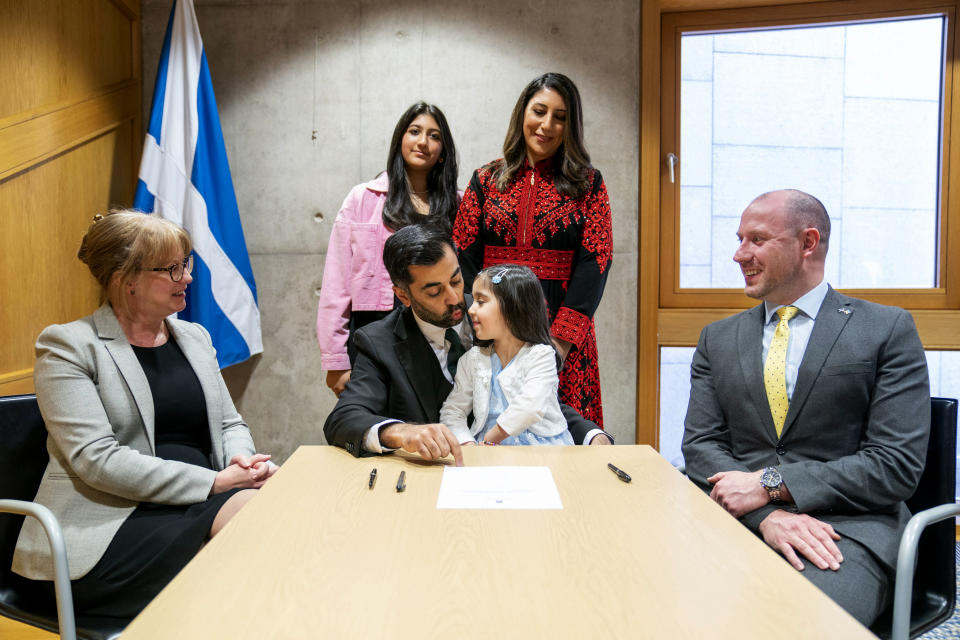 Newly elected leader of the Scottish National Party, Humza Yousaf, center, signs the nomination form to become First Minister for Scotland, as his wife Nadia El-Nakla, standing background right, daughter Amal, 3, and step-daughter Maya (back left), stand behind him, with proposer Shona Robison, left, and seconder Neil Gray, at the Scottish Parliament in Edinburgh, Scotland, Tuesday March 28, 2023. Scotland’s governing Scottish National Party on Monday elected Humza Yousaf as its new leader, the first person of color and the first Muslim to serve as Scotland’s first minister, after Sturgeon unexpectedly stepped down last month. ( Jane Barlow/PA via AP)