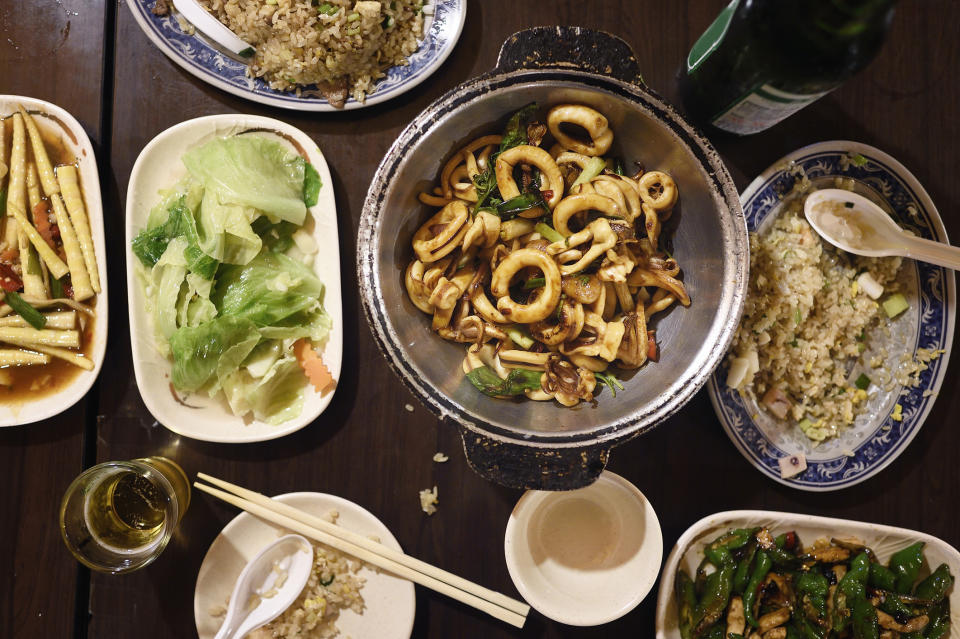 A table with various Chinese dishes: a pot of calamari with vegetables, fried rice, stir-fried vegetables, and a green bottle