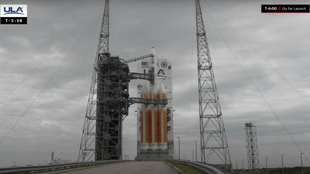  An orange and white rocket stands on the launch pad under cloudy gray skies. 