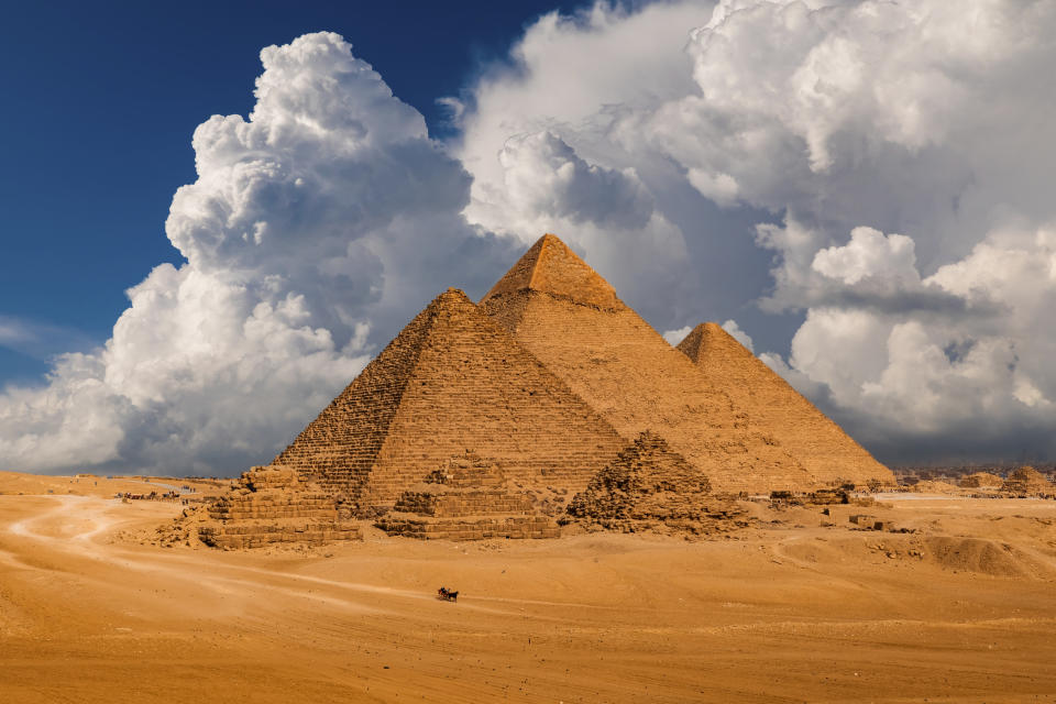 The image shows the Pyramids of Giza in Egypt with a backdrop of dramatic clouds in the sky