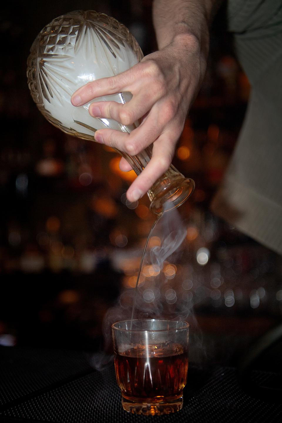 August Henson pours a Fall Fashion cocktail from a bottle filled with pip tobacco smoke, April 4, 2024, at The Crow and Quill.