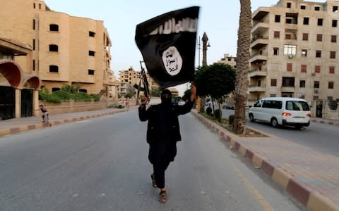 A member loyal to the Islamic State in Iraq and the Levant (ISIL) waves an ISIL flag in Raqqa June 29, 2014 - Credit: Reuters