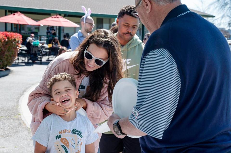 Selina Dickerson holds her son, Christoper, 5, as he smiles waiting to get a plate form Ken Morton Sr., CEO Morton Golf, right, in the pancake line during the Haggin Oaks Easter Egg Hunt on Sunday, April 9, 2023, in Sacramento.