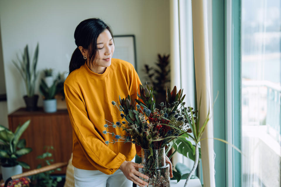 Person standing indoors holding a bouquet of dried plants next to a window