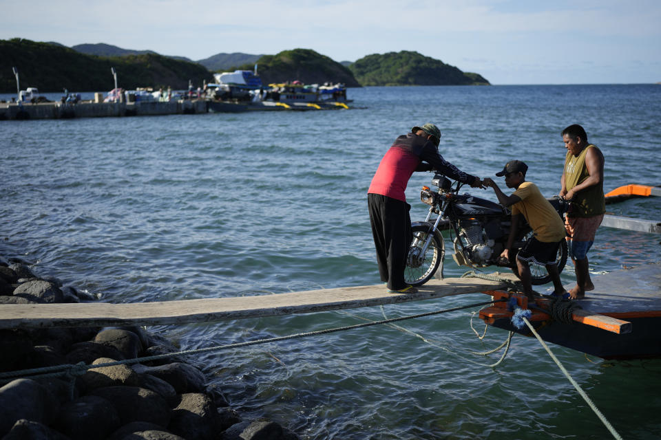 Workers push a motorcycle along a wooden plank at the port of the coastal town of Santa Ana, Cagayan province, northern Philippines on Tuesday, May 7, 2024. The United States and the Philippines, which are longtime treaty allies, have identified the far-flung coastal town of Santa Ana in the northeastern tip of the Philippine mainland as one of nine mostly rural areas where rotating batches of American forces could encamp indefinitely and store their weapons and equipment within local military bases under the Enhanced Defense Cooperation Agreement, or EDCA. (AP Photo/Aaron Favila)