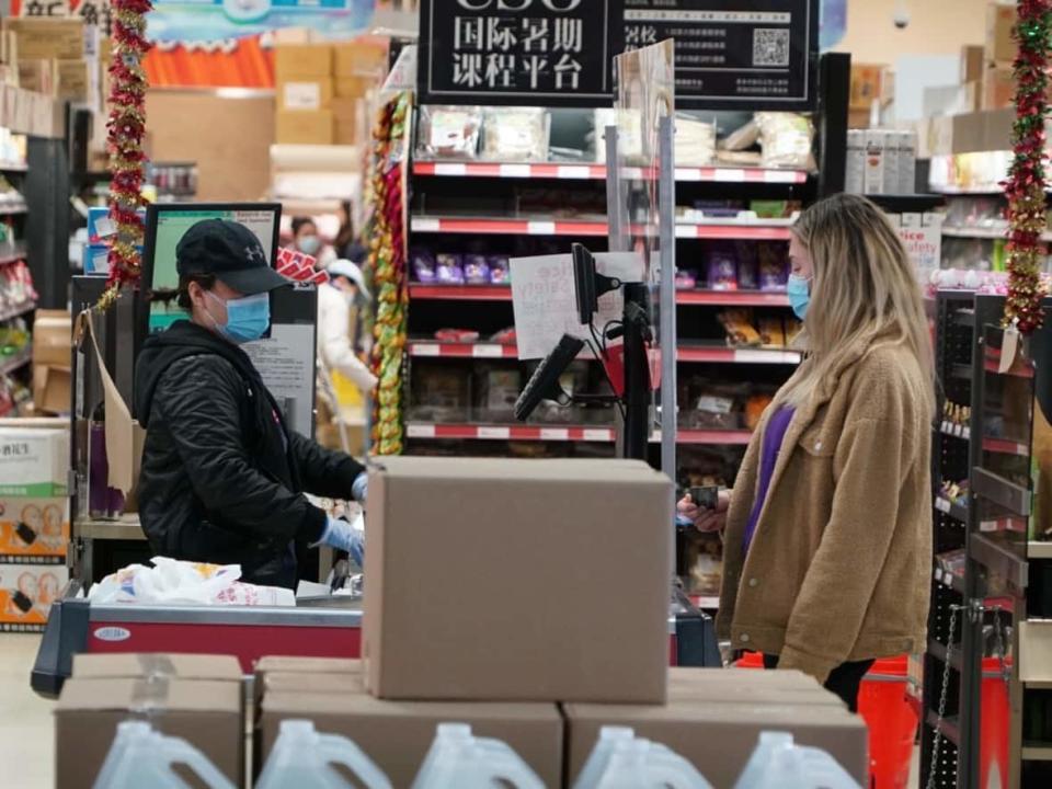 A woman in a surgical mask pays for her groceries at a store checkout in London, Ont. Nearly two years into the pandemic, thousands of Canadian&#xa0;front-line workers who are unable to do their job from home&#xa0;continue to put themselves at greater risk of contracting COVID-19. (Colin Butler/CBC - image credit)
