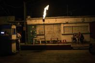 In this May 23, 2019 photo, Richard Montano eats "Tumbarrancho" arepas with his son Reinel Montano, 13, illuminated by a torch known in Maracaibo as a "Mechurrio" during a black out in Maracaibo, Venezuela. The "Mechurrio" belongs to the arepa vendor, and he uses it as a way to attract customers in Maraciabo's darkened streets. (AP Photo/Rodrigo Abd)