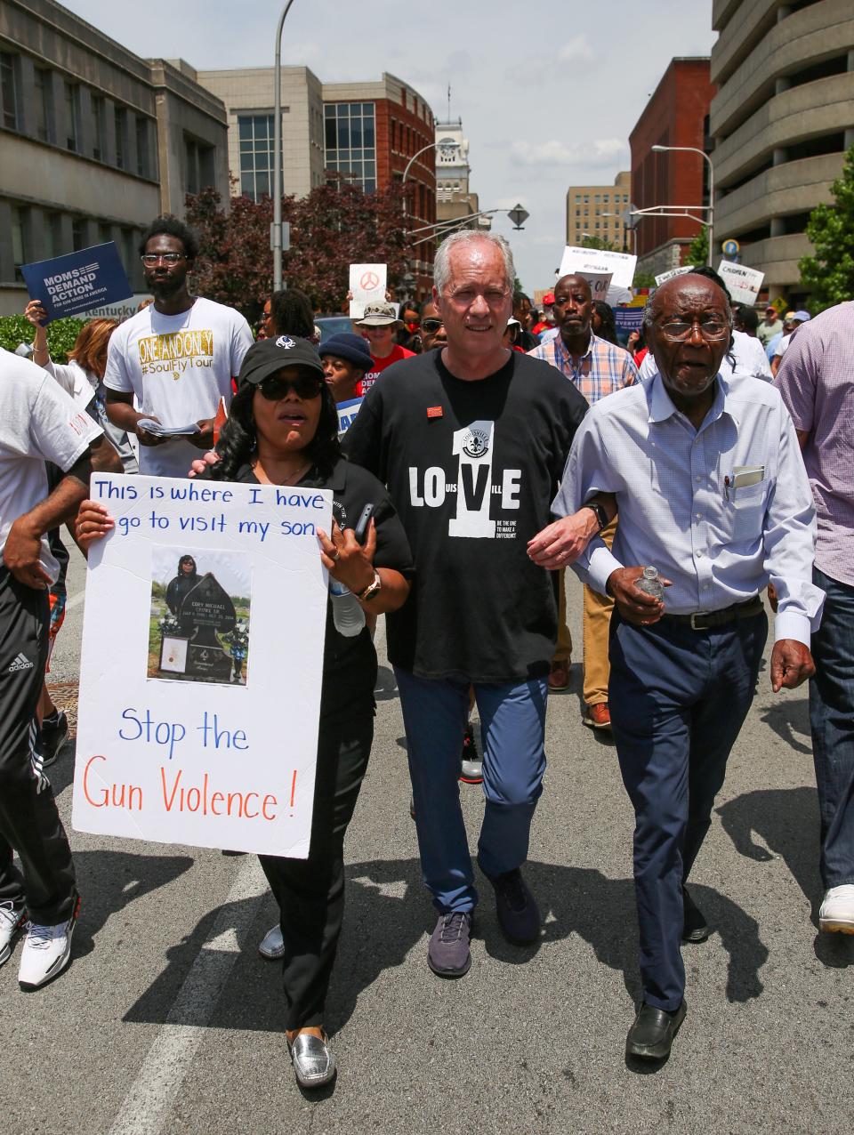 Mayor Greg Fischer locks arms with Rose Smith and Reverend Charles Elliott during a march protesting gun violence in downtown Louisville, Kentucky on June 11, 2022. 