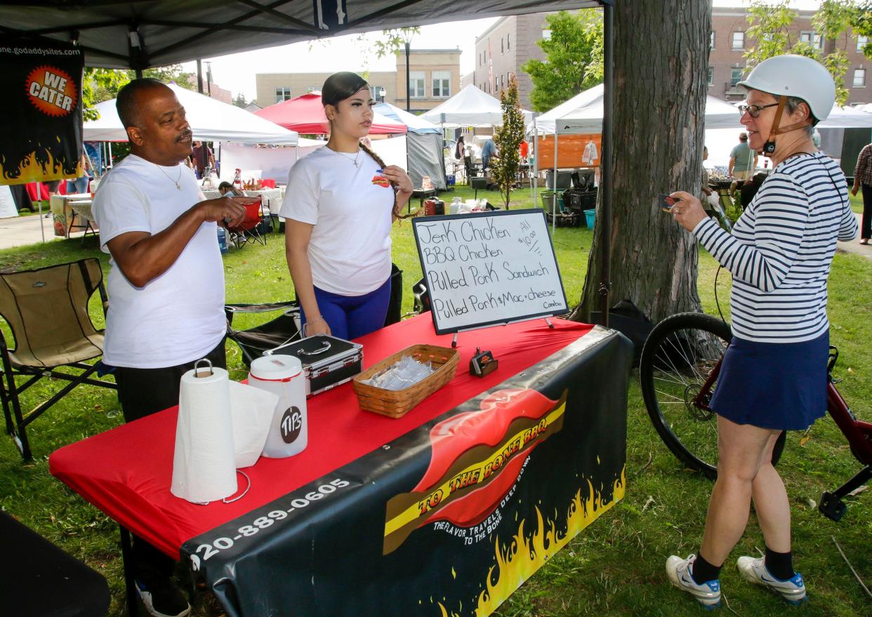 Robert Berry, Sr., left, explains his catering capabilities to Kati Fritz-Jung, right, of Sheboygan, at the SCIO Farmer’s Market at Fountain Park, Saturday, August 12, 2023, in Sheboygan, Wis.  In the center is Berry’s daughter Bridgit.