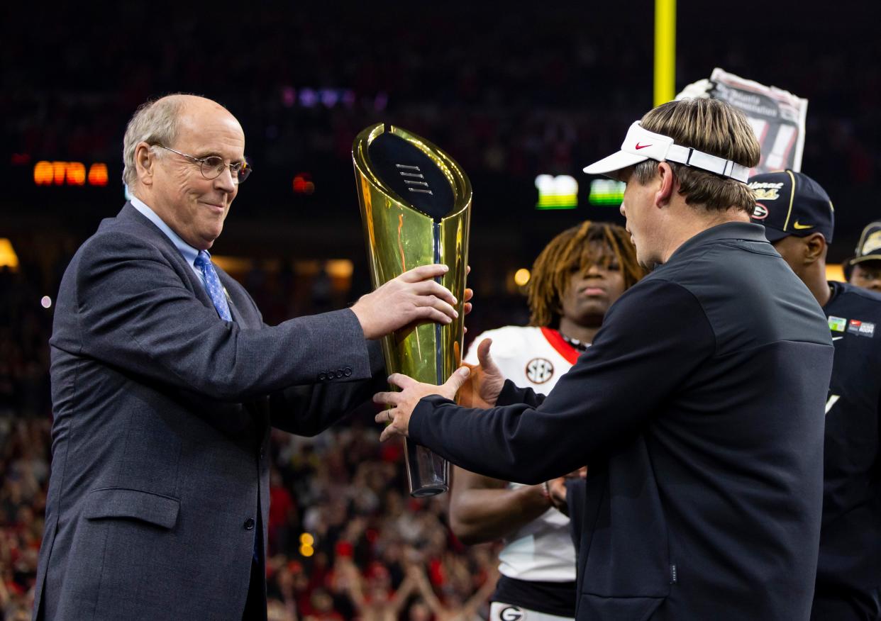 Executive director of the College Football Playoff Bill Hancock hands the championship trophy to Georgia Bulldogs head coach Kirby Smart (right) after defeating the Alabama Crimson Tide in the 2022 CFP college football national championship game at Lucas Oil Stadium.