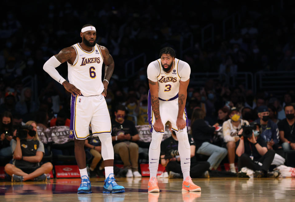 LeBron James, with his hands on his hips, and Anthony Davis, bent over with his hands on his knees, stand next to each other on the court.