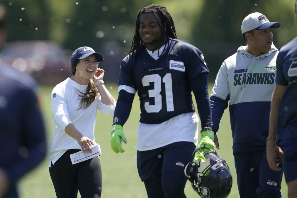 Amanda Ruller, left, who is currently working as an assistant running backs coach for the NFL football Seattle Seahawks through the league's Bill Walsh Diversity Fellowship program, walks with running back DeeJay Dallas (31) during NFL football practice on May 31, 2022, in Renton, Wash. Ruller's job is scheduled to run through the Seahawks' second preseason game in August. At right is Seahawks run game coordinator and running backs coach Chad Morton. (AP Photo/Ted S. Warren)