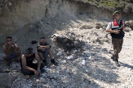 A Turkish gendarme stands guard next to Iranian migrants at a beach in Cesme, near the Aegean port city of Izmir, Turkey, August 11, 2015. REUTERS/Sait Serkan Gurbuz