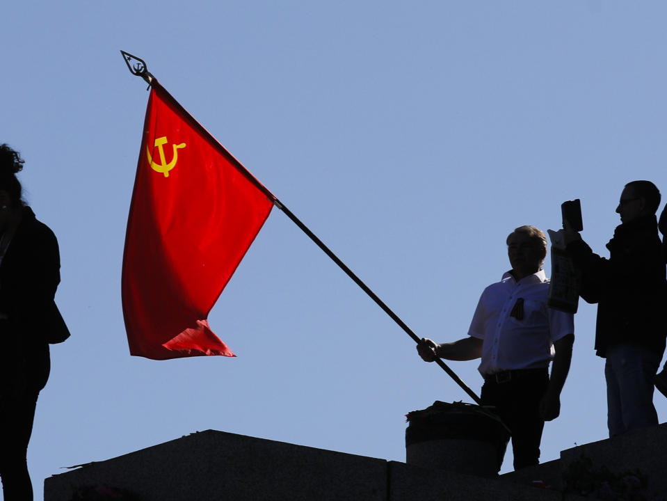 FILE - In this file photo dated Saturday, May 9, 2020, a man holds a Soviet flag during a ceremony at the Soviet War memorial to mark the 75th anniversary of Victory Day at the district Treptow in Berlin, Germany. An influential committee of British lawmakers plans to publish its findings Tuesday July 21, 2020, reporting on Russian interference in British politics, amid criticism the government delayed its release for more than six months to shield Prime Minister Boris Johnson and his Conservative Party from embarrassment. (AP Photo/Markus Schreiber, FILE)