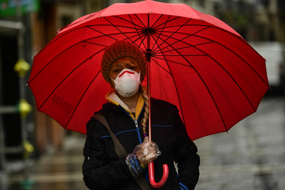 A woman wearing a mask protects herself from the rain with an umbrella, in Pamplona, northern Spain, Monday, March 16, 2020. After deploying the army to the streets and to clean train stations, ordering 46 million to stay at home and taking over control of private hospitals, the Spanish government is considering now closing the country's borders to halt the spread of the coronavirus. For most people, the new coronavirus causes only mild or moderate symptoms. For some, it can cause more severe illness, especially in older adults and people with existing health problems. (AP Photo/Alvaro Barrientos)