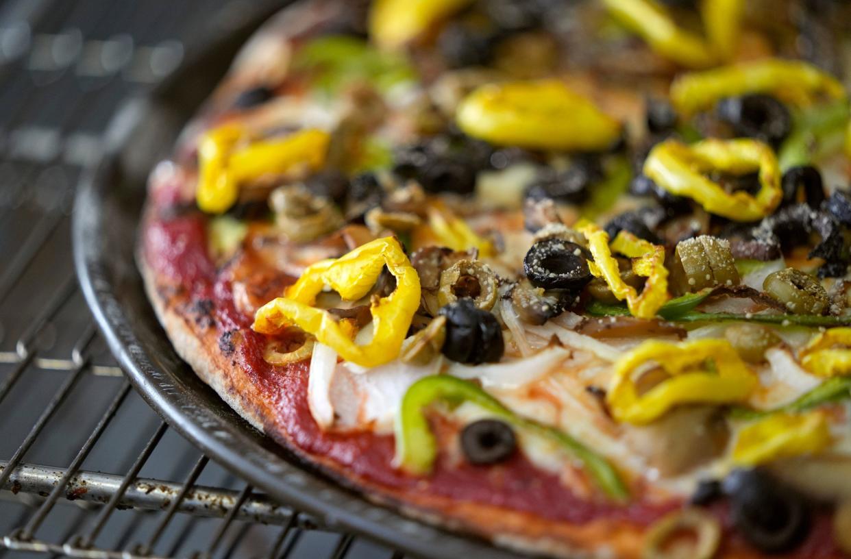 A build-your-own veggie pizza comes out of the oven at Terita's Pizza, featuring green and black olives, banana and green peppers, and onions.