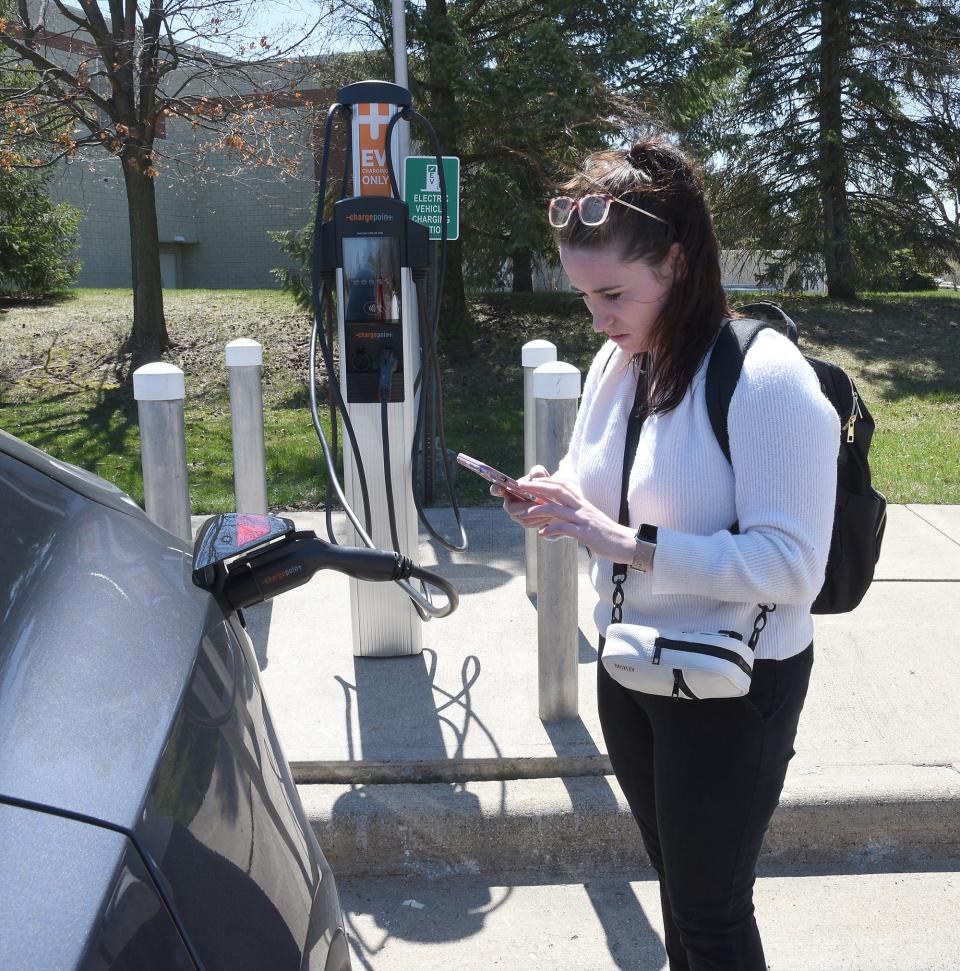 Katie Maller, business development associate and marketing coordinator for EVunited, uses an app on her phone to make sure the new EV charging station connects to her Telsa electric car at Monroe County Community College in front of the La-Z-Boy Center.