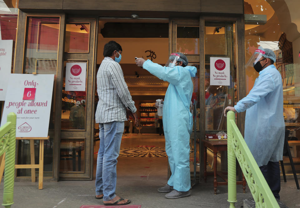 An Indian security personnel wearing protective gear checks the temperature of a customer before allowing him to enter a sweet shop in Hyderabad, India, Friday, June 5, 2020. The more than two-month-old lockdown is now largely being enforced only in high-risk areas, known as containment zones. The government has partially restored train service and domestic flights and allowed the reopening of shops and manufacturing. (AP Photo/Mahesh Kumar A.)