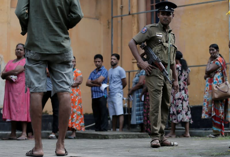 A police officer looks on as people stand in a line to cast their vote during the presidential election in Colombo