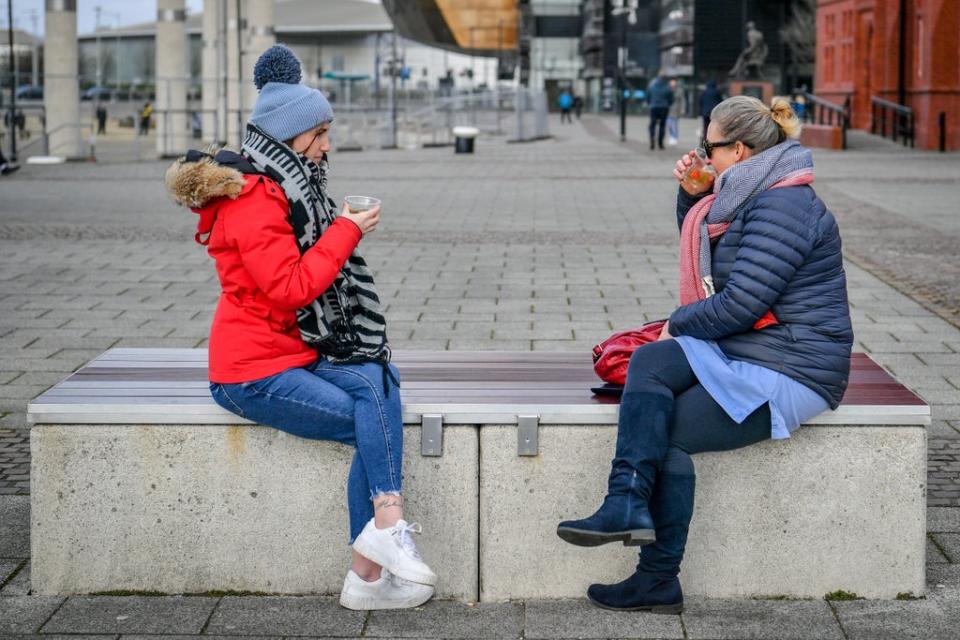 Two members of the public enjoy a socially distanced coffee in Cardiff during the last national lockdown (PA)