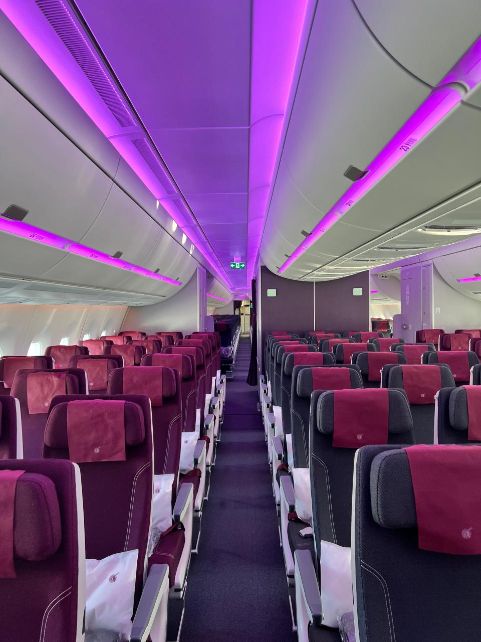 A view down the aisle of economy class in an A350, with purple accent lighting and burgundy and black seats.