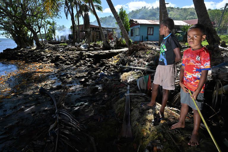 Esta fotografía tomada el 13 de diciembre de 2022 muestra a jóvenes afuera de sus casas frente a la playa amenazados por la erosión costera en la ciudad de Veivatuloa en Fiji