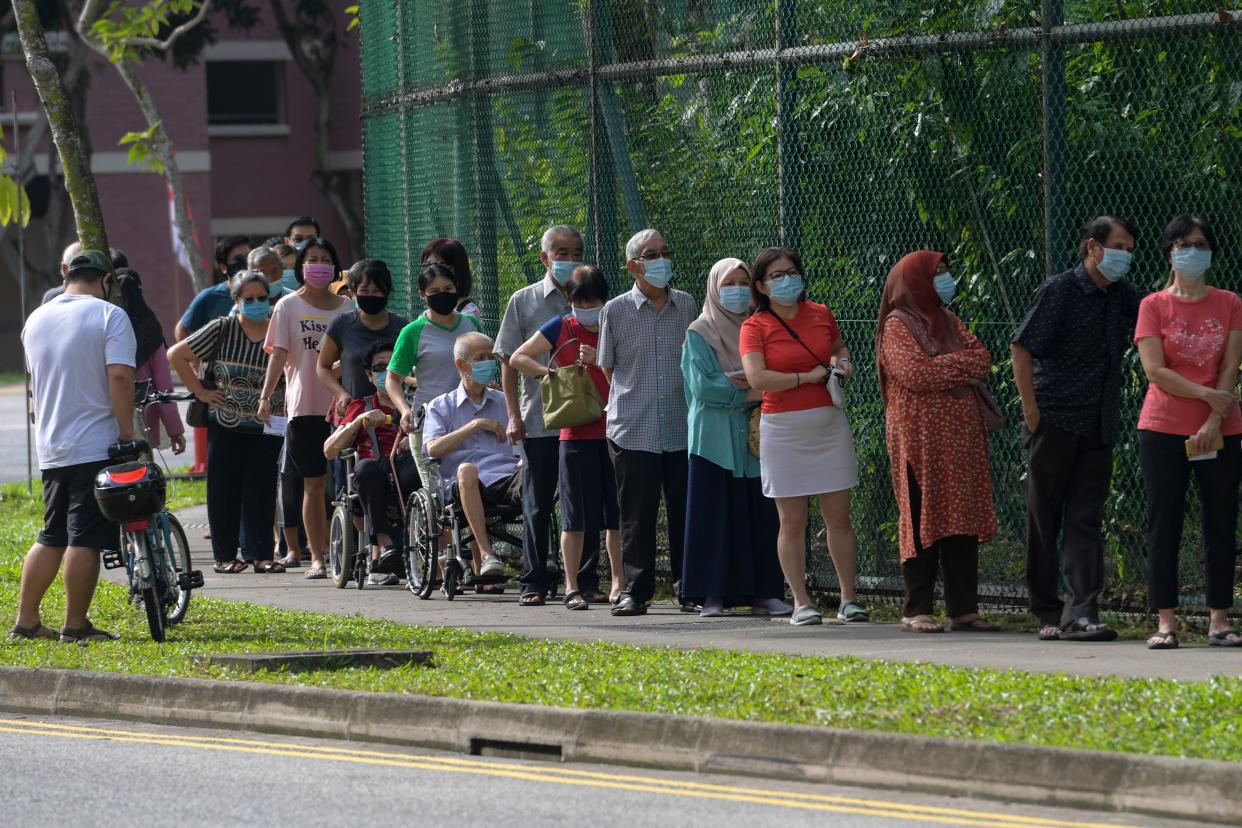 Voters wearing face masks wait to enter a school, temporarily used as a polling station, to cast their ballots during the general election in Singapore on July 10, 2020. - Wearing masks and gloves and being careful to observe social distancing, Singaporeans voted in a general election on July 10 as the city-state struggles to recover from a coronavirus outbreak. (Photo by Roslan RAHMAN / AFP) (Photo by ROSLAN RAHMAN/AFP via Getty Images)