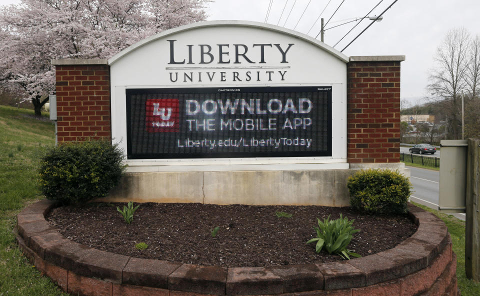 FILE - In this March 24 , 2020, file photo, a sign marks the entrance to Liberty University in Lynchburg, Va. The university, led by Jerry Falwell Jr., is pushing for criminal trespassing charges to be lodged against two journalists who pursued stories about why the evangelical college has remained partially open during the coronavirus outbreak. (AP Photo/Steve Helber, File)