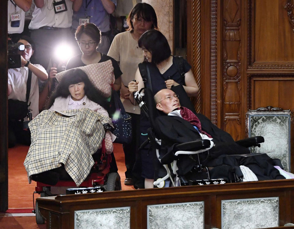 Two newly-elected lawmakers, Yasuhiko Funago, right, and Eiko Kimura, in wheelchairs are helped to arrive for an extraordinary session of the parliament's upper house in Tokyo Thursday, Aug. 1, 2019. Japan’s parliament convened after elections and a minor renovation at the upper house. Funago, who has Amyotrophic Lateral Sclerosis, a progressive neurological disease known as ALS, and Kimura who has cerebral palsy, won the July 21 elections at the less-powerful of the two chambers, representing an opposition group. (Muneyuki Tomari/Kyodo News via AP)