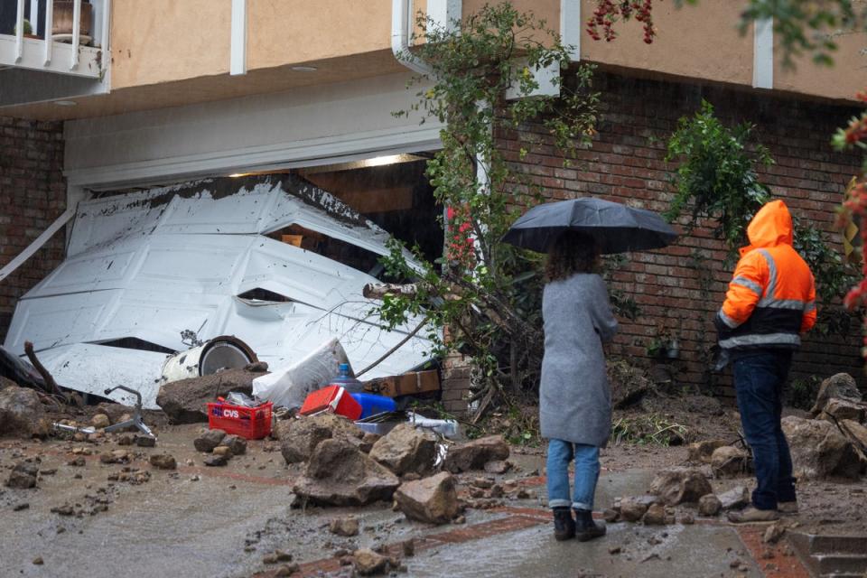 Two people stand outside a home damaged by a landslide in Los Angeles, California on Monday (AFP via Getty Images)